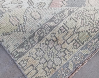 May include: A vintage-style rug with a folded corner, showcasing a detailed geometric pattern. The rug features a palette of soft colors, including cream, gray, pink, and green. The design incorporates intricate shapes and borders, creating a classic, textured look.