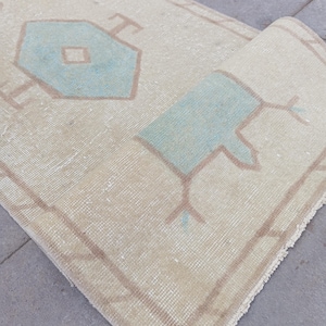 Könnte beinhalten: Ein hellbeiger Teppich mit einem geometrischen Muster in hellblau. Der Teppich hat einen Fransenrand.