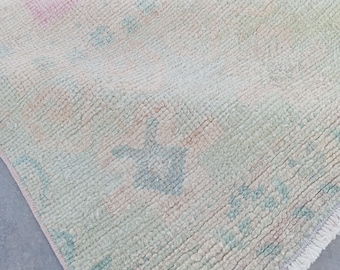 May include: A light-colored, textured rug with a folded section. The rug features a pastel color palette with pink, blue, and green accents. The edges are finished with a fringe.
