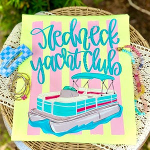 Peut inclure: Un t-shirt jaune néon avec des rayures verticales roses et jaunes. Le t-shirt présente les mots "Redneck Yacht Club" en écriture turquoise au-dessus d'une illustration de bateau ponton. Accessoires : pince à cheveux à carreaux bleus et colliers de perles.