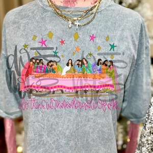May include: A gray, short-sleeved t-shirt featuring a colorful illustration of the Last Supper. The graphic includes figures seated at a table with the text "do this in remembrance of me". The shirt is styled with layered necklaces.