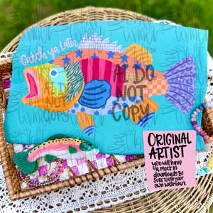 May include: A turquoise t-shirt with a vibrant cartoon fish design, featuring the text "Catch ya Later." The fish is decorated with orange, pink, blue, and purple patterns. A small decorative fish is also present. The text "AL DO NOT COPY" is also visible.