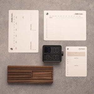 May include: A set of stationery including a vertical Weekly Tracker sheet, a horizontal Habit Tracker sheet, and a 1-3-5 System planner sheet. A black digital timer with a side dial and a rectangular wooden stand with horizontal grooves.