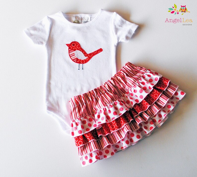 May include: A white bodysuit with a red bird applique and a red and white polka dot skirt with ruffles.