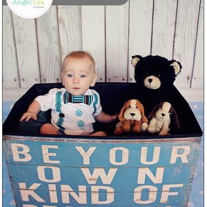 May include: A blue and white wooden box with the text "Be Your Own Kind of Beautiful" printed on it. A baby boy is sitting in the box with a blue bow tie and a white shirt with blue polka dots. There are three stuffed animals in the box: a black bear, a brown dog, and a white dog.