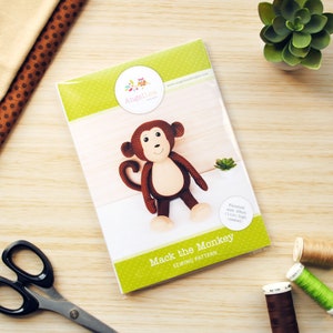 May include: A sewing pattern for a brown plush monkey toy named Mack the Monkey. The pattern is printed on a white sheet of paper with a green background and a small owl logo. The finished size of the monkey is 11 inches high when seated.