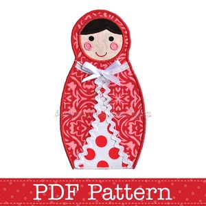 May include: Red and white fabric applique of a Russian nesting doll, or matryoshka doll, with a white lace trim and polka dots. The doll has a red and white floral pattern and a white bow. The text "PDF Pattern" is below the doll.