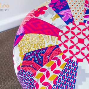 May include: A round, multi-colored patchwork pouf with a white background and various floral and geometric patterns. The pouf is made of fabric and has a circular shape.