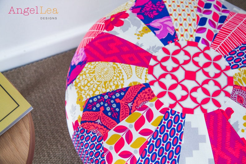 May include: A round, multi-colored patchwork pouf with a white background and various floral and geometric patterns. The pouf is made of fabric and has a circular shape.