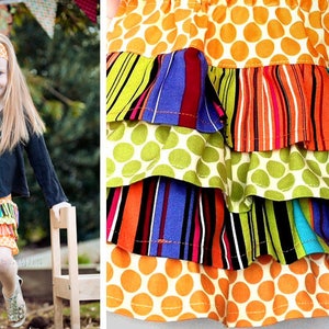 May include: A multi-layered skirt with a bright, colourful pattern. The skirt features a top layer of orange fabric with white polka dots, followed by layers of green polka dots, striped fabric, and more polka dots. The skirt is a fun and playful piece of clothing.