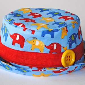 May include: A blue and red children's hat with a yellow button. The hat is decorated with a pattern of colorful elephants.