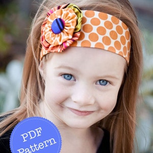 May include: A young girl with long, red hair is wearing a headband with a large, colorful flower and orange polka dots. The headband is made of fabric and has a button in the center of the flower. The girl is smiling and looking at the camera. The text "PDF Pattern" is on a blue circle in the lower left corner of the image.