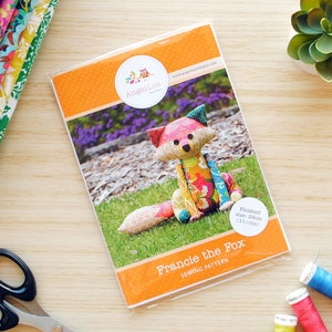 May include: A sewing pattern for a colorful fox plush toy named "Francie the Fox". The pattern is printed on orange paper with a white circle that says "Finished size: 20cm (11 in)".