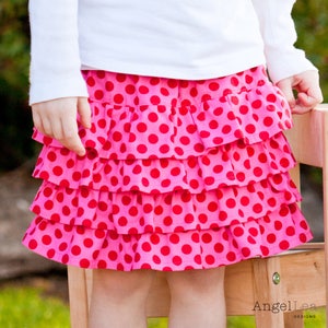 May include: A pink skirt with red polka dots and multiple ruffles. The skirt is made of a soft, comfortable fabric.
