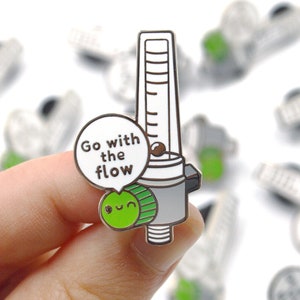 May include: A silver and green enamel pin featuring a cartoon character with a gauge and the text "Go with the flow".