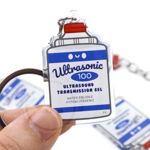 May include: A clear acrylic keychain shaped like a bottle of ultrasound transmission gel. The bottle is blue and white with red accents and the text "Ultrasonic 100 Ultrasound Transmission Gel Water Soluble Hypoallergenic" printed on the front.