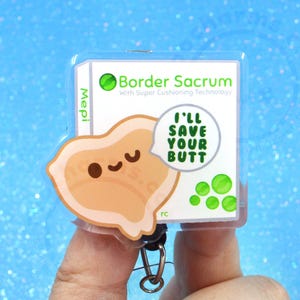 Pu&ograve; includere: Un porta badge quadrato in acrilico con sfondo bianco e il testo Border Sacrum With Super Cushioning Technology e Mepi. Un personaggio a forma di osso sacro color marrone chiaro in stile cartone animato con un viso sorridente tiene un fumetto con I'LL SAVE YOUR BUTT.