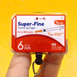 May include: A rectangular badge featuring a red and white design with the text "Super-Fine Insulin Syringes." The badge includes a syringe illustration and reads "6 31G mm" and "100 Sterile Single Use Syringes."