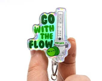 Op de afbeelding: Een holografische acryl badgehouder met een groene afbeelding van een zuurstofdebietmeter en de tekst "GO WITH THE FLOW" in dikke groene letters. Het ontwerp bevat een kleine groene knop met een lachend gezichtje en een doorzichtige plastic bevestigingsstrip.