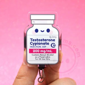 May include: A badge reel shaped like a medicine vial with a smiling face. The label reads Testosterone Cypionate INJECTION, USP 200 mg/mL, Rx Only, and contains Benzyl Alcohol as a Preservative For IM Use Only. The design features a white background.