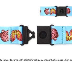 May include: A blue lanyard with a white background and a repeating pattern of pink brains and lungs. The lanyard has a black plastic breakaway clasp.