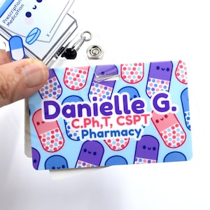 May include: A name badge with a light blue background featuring cartoon pills in pink, purple, and blue. The badge reads "Danielle G. C.Ph.T, CSPT Pharmacy". A second badge with a cartoon pill is also visible.