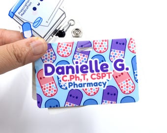 May include: A name badge with a light blue background featuring cartoon pills in pink, purple, and blue. The badge reads "Danielle G. C.Ph.T, CSPT Pharmacy". A second badge with a cartoon pill is also visible.