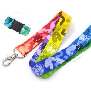 May include: A rainbow-colored fabric lanyard featuring a repeating pattern of cute, smiling microorganisms and geometric shapes. The strap includes a silver-toned metal lobster clasp and a black plastic breakaway buckle, with the text roocharms printed.
