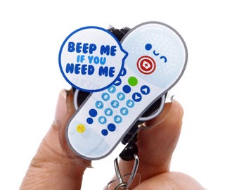May include: A badge reel featuring a white pager-shaped design with blue buttons and a red medical cross icon. A blue speech bubble attached to the top displays the text BEEP ME IF YOU NEED ME in blue capital letters against a white background.