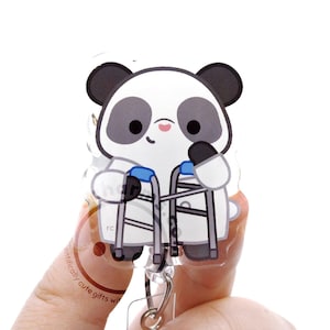 May include: A clear acrylic badge reel featuring a cartoon panda with black and white fur, a small pink nose, and a subtle smile. The panda is depicted standing and holding a pair of grey medical crutches with blue accents on the handles.