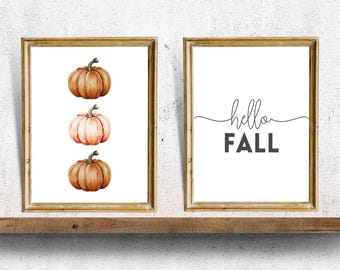 May include: Two framed prints, one with a watercolor illustration of three pumpkins in shades of orange and pink, and the other with the text "hello fall" in black cursive.