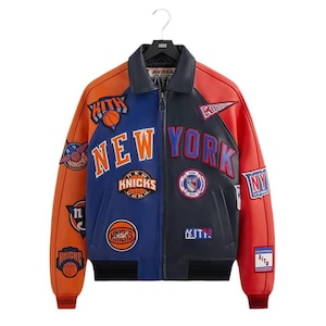 Pode incluir: Uma jaqueta universitária de couro multicolorida com painéis laranja, azuis e azul-marinho escuro. A frente apresenta emblemas bordados incluindo o texto NEW YORK, KNICKS e KITH, juntamente com gráficos de basquete e logotipos de equipes.