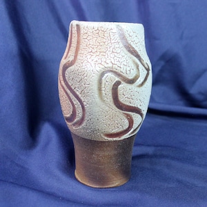 May include: A ceramic vase with a textured, off-white surface and brown, wavy lines. The vase has a rounded body and a slightly flared opening.