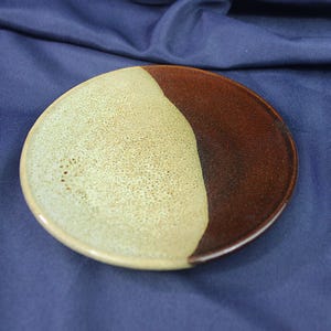 May include: A ceramic plate with a brown and beige glaze. The plate is divided in half, with one side being brown and the other side being beige.