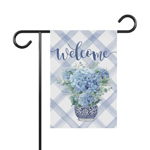 May include: A blue and white welcome garden flag with a blue hydrangea bouquet in a blue and white vase on a white and blue gingham background.