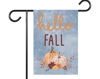 May include: A blue and white garden flag with the text "hello fall" in orange and red. The flag features a watercolour-style design with two pumpkins and autumn foliage.