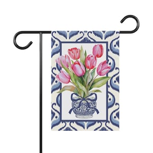 Può includere: Una bandiera da giardino con un'illustrazione ad acquerello di tulipani rosa in un vaso blu e bianco. La bandiera ha un bordo a motivi blu e bianchi ed è esposta su un supporto in metallo nero.