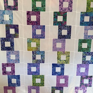 May include: A handmade quilt featuring a repeating pattern of squares within squares. The squares are made of various patterned fabrics in shades of green, purple, blue, and white. The quilt is made of white fabric.