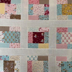 May include: A patchwork quilt top featuring nine square blocks separated by white sashing. The blocks contain various fabric patterns including pink, blue, brown, and yellow colours with prints of horseshoes, cowboy boots, flowers, and children.