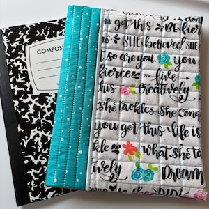 May include: A white quilted notebook cover with black text that reads "You got this - Be Fierce - Live Creatively - She Tackles, She Conquers - You got this - Life is what she makes it - Dream Big". The cover has a turquoise and white patterned border.