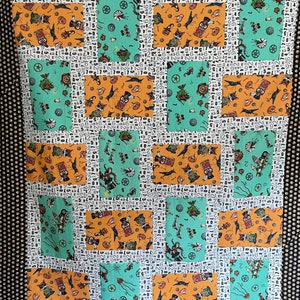 May include: A quilt made of fabric squares with a steampunk theme. The squares feature a variety of images, including gears, clocks, and other mechanical elements. The fabric is a mix of orange, teal, and white.