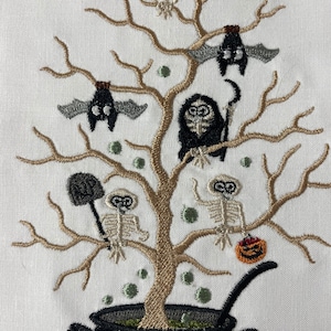 May include: Embroidered kitchen towel with a black cauldron, a brown tree with skeletons, bats, and a pumpkin. The cauldron is filled with green liquid and has steam coming out of it.