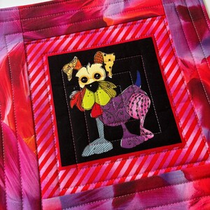 Peut inclure: Un set de table matelassé avec un motif de chien coloré. Le chien a un visage jaune, un corps violet et des détails bleus et verts. Le set de table présente un motif floral rouge et rose et une bordure rayée.