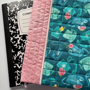 May include: A teal blue fabric phone book cover with a pink quilted border. The cover features a repeating pattern of vintage rotary phones and flowers.