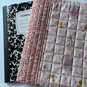 May include: A black and white composition notebook with a floral and sewing themed fabric cover. The cover has a quilted design with various sewing-related images, including scissors, needles, and thread.