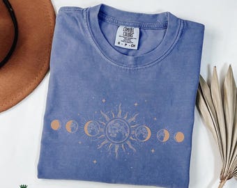 May include: A blue t-shirt with a sun and moon graphic. The graphic features a sun with a face and a crescent moon with stars. The text "COMFORT COLORS" is on the tag.