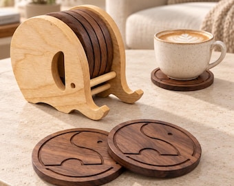 May include: A light-colored wooden elephant-shaped holder containing several dark brown circular wooden coasters. Two additional dark brown circular coasters with an engraved elephant silhouette are placed on the surface, one supporting a ceramic mug.