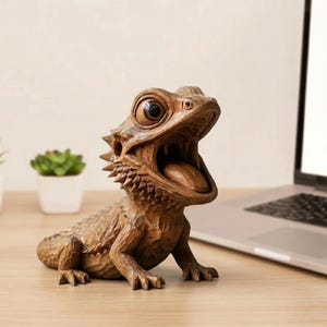 May include: A detailed wooden sculpture of a bearded dragon with its mouth open, tongue visible. The reptile is carved from light brown wood, showcasing intricate details. The sculpture is positioned on a wooden surface.