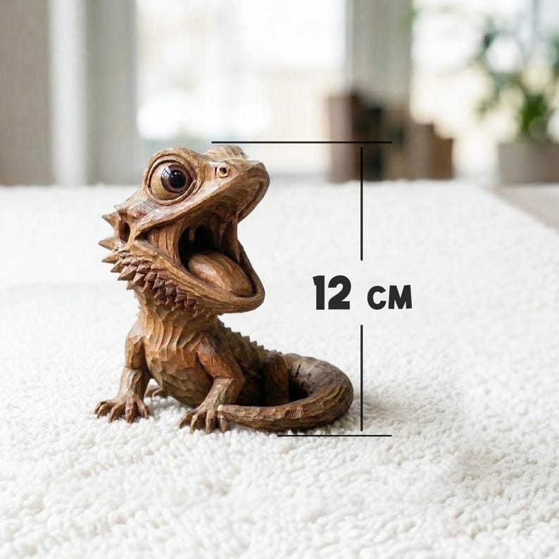May include: A detailed wooden sculpture of a bearded dragon with its mouth open, revealing its tongue. The sculpture is approximately 12 cm (4.7 inches) tall and is set against a soft, white background. The lizard's scales and features are intricately carved.