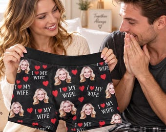 May include: Black boxer briefs featuring a repeating pattern of a woman's face, red hearts, and the white text "I MY WIFE". The garment has a wide black elastic waistband and is constructed from a soft, stretchable fabric with a fitted silhouette.